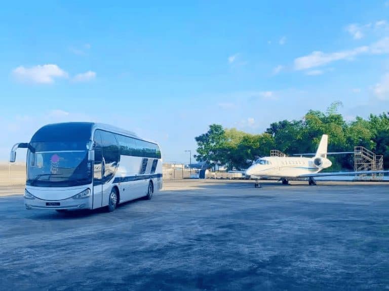 Modern bus and private jet at airport tarmac for luxury transportation services.